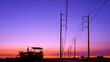 Silhouette of bulldozer tractor with row of electric poles in countryside area against colorful twilight sky background