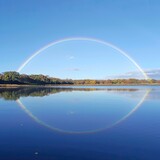 Fototapeta Tęcza - tranquil lake reflecting a full arc rainbow under a clear sky