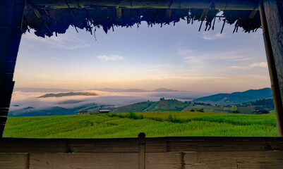 Wall Mural - a view of a field with a foggy sky and mountains in the background. the sky is a mix of blue and ora