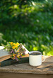 Enamel mug with herbal tea, fresh useful flowers and herbs, books on wooden table in garden, natural background. healthy beverage, Flavor herbal tea from organic natural ingredients.