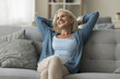 © fizkes - Relaxed happy older woman spend peaceful retirement at home, leaned on cozy sofa with hands behind head, feel satisfied, enjoy serenity and leisurely lifestyle, having lazy weekend. Comfort life, rest