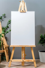 A white blank canvas on an easel with white flowers and greenery around on a plain background..Empty white board for the guest list or photo. empty white board for drawing