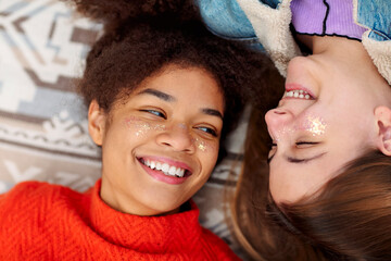 Wall Mural - Two young diverse girlfriends looking at each other with love while resting on plaid outdoors