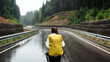Back view of female hiker with yellow backpack walking on asphalt road with beautiful mountains around. Concept of people and leisure activity.