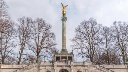 Wall Mural - Front view of famous Peace Column with golden Angel of Peace statue (Friedensengel) timelapse, people and public park in the Bavarian capital near Isar river. Germany, Munich, Bogenhausen