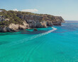 Panoramic view of the beautiful Macarella bay with a boat crossing the turquoise waters on Menorca in balearic islands in Spain