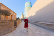Young woman in red dress and hat walking in front of blue Kalta minor minaret in Itchan Kala ancient city of Khiva in Uzbekistan.
