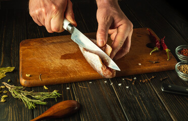 Wall Mural - The cook hands use a knife to cut frozen hake fish on a wooden cutting board. National fish dish prepared in a restaurant according to a unique recipe