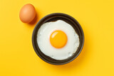 Fototapeta Desenie - fried egg with a whole yolk in a frying pan on a yellow background, top view, minimalism