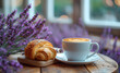 A cup of aromatic coffee with a croissant on a background of lavender flowers
