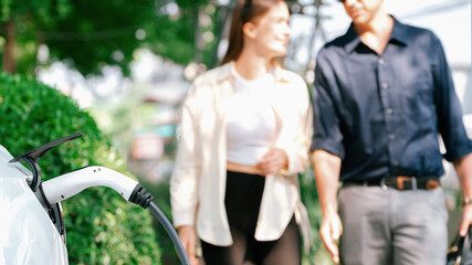 young couple recharge electric car battery from charging station in green city park in springtime. r