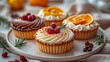   A white plate holds cupcakes, each topped with frosting and garnished with orange slices and cranberries