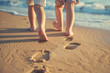© IQRA - A cute sister and brother's feet walking on a sandy beach, leaving behind footprints as memories of their journey.