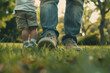 A cute father and baby's little shoes side by side, taking their first steps on a grassy field.