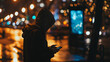 a moment in an urban setting during nighttime. The focal point is a person standing on a sidewalk, engrossed in their phone