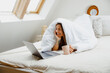 Woman in comfortable linens, happy on bed with laptop and coffee