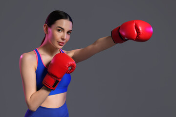 Canvas Print - Beautiful woman wearing boxing gloves training in color lights on grey background