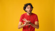 An attractive man with curly hair, dressed in red T-shirt,  listens and strongly disagrees while looking at camera isolated on yellow background in studio