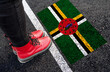 a woman with a boots standing on asphalt next to flag of Dominica and border