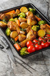 Healthy food baked chicken drumstick with broccoli, potatoes, tomatoes and carrots close-up on a pan on the table. Vertical