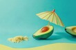 A ripe avocado cut in half lies on the sand with a parasol. Shades of blue as a background. Minimal concept.