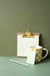 Workspace notepad binder clip, pen, mug cup on green desk. khaki wall background