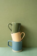 Stack of ceramic mug cups on green table. khaki wall background