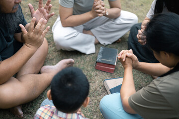 Wall Mural - Young woman held her mother's hand in prayer, surrounded by their outdoor community, where love and family life flourished through shared moments of prayer and support. Group christian pray concept.