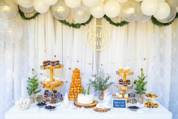 Cakes and sweets on a table with white balloons hanging on the wall at a baby shower girl party