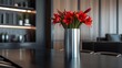A sleek, cylindrical stainless steel vase on a sleek black dining table, with red amaryllis flowers