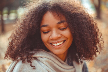 Wall Mural - Cute autumn portrait of young happy curly african american woman enjoying fall season in park