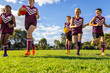 © Austockphoto - schoolkids running towards the camera on green grass with footballs