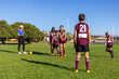 © Austockphoto - children at football training with a female coach on green grass oval with blue sky