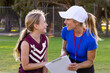 © Austockphoto - female sports coach interacting with young girl football player with clipboard