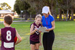 © Austockphoto - young girl with sports coach looking at clipboard on playing field