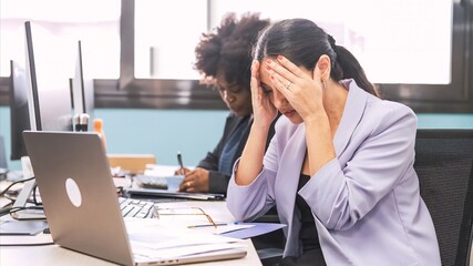 Overworked businesswoman sitting with head in hands at laptop desk in office