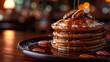   A stack of pancakes atop a black plate, coated in syrup, with a pretzel on the side