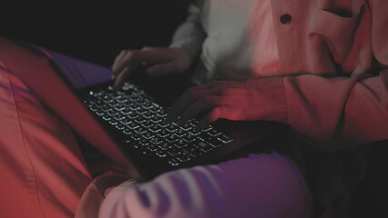 Close up of freelancer's developer hands typing program code on laptop keyboard in coworking. businesswoman sitting on the floor in a dark room with red light and typing on a laptop