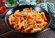 Classic italian pasta penne arrabbiata with vegetables on wooden table. Penne pasta with sauce arrabbiata. Top view, overhead