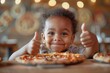 A young boy with curly hair, giving thumbs up in approval of the pizza in front of him