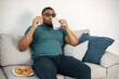 Black guy sitting on a couch in living room drinking a tea and eating a cookies