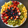 An aerial shot of a fresh fruit salad arranged in a geometric pattern, showcasing a colorful assortment of sliced strawberries, blueberries, kiwi, pineapple, and grapes on a white serving platter.