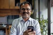 © Andrei - Smiling mature Indian businessman holding smartphone in office and looking at the camera.