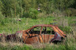 Rusty and broken red abandoned car in the outdoors. Old abandoned rusty car without wheels on the side of the road