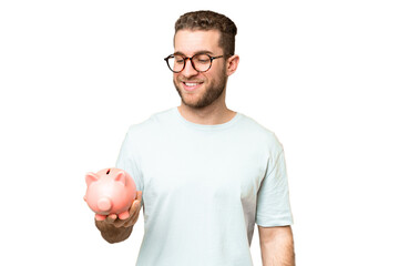 Wall Mural - Young man holding a piggybank over isolated chroma key background with happy expression