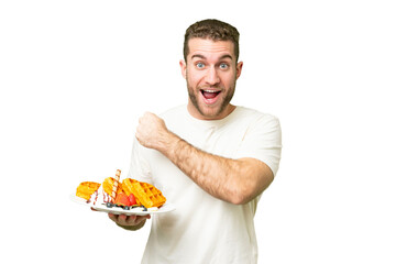 Wall Mural - Young handsome blonde man holding waffles over isolated chroma key background celebrating a victory