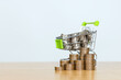 Shopping cart and a pile of coins on wood table. Shopping cart full of coins over for advertising with copy space