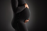 Fototapeta Sawanna - Elegant Pregnant Woman Embracing Her Belly in Striped Dress