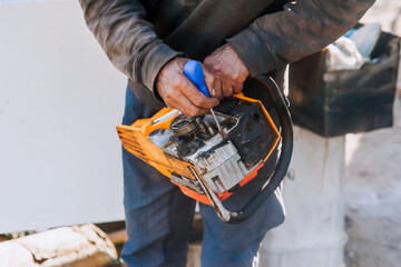 A man, a professional mechanic, repairs an electric saw with a special tool with a screwdriver, performing maintenance in the workshop.