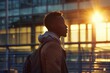 Young man with backpack looking hopeful against the backdrop of an airport at sunrise, signaling new beginnings and travel aspirations.

